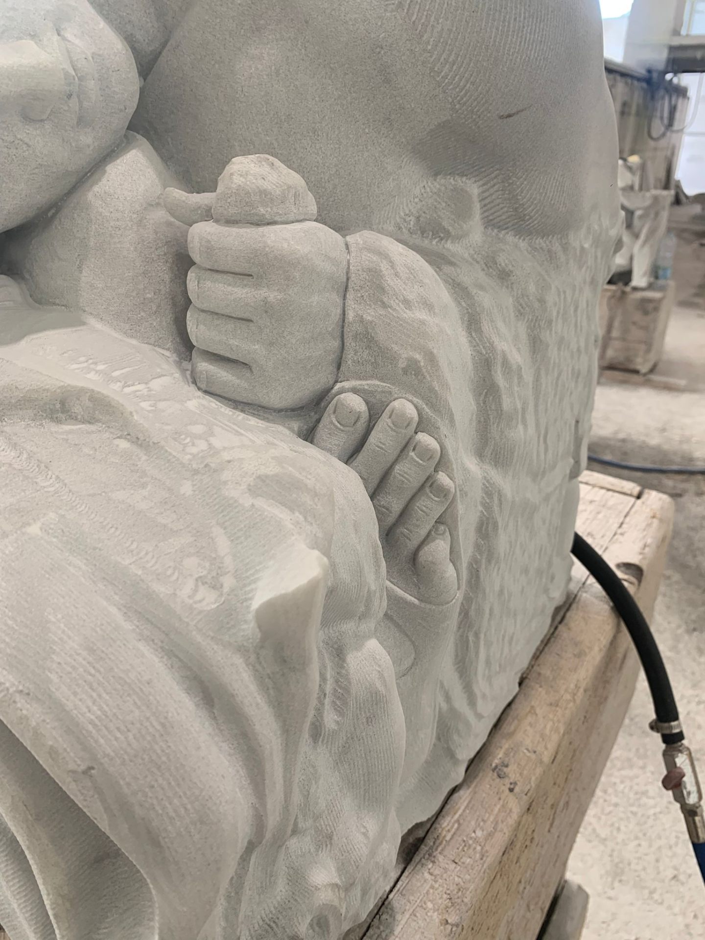 Tight detail of a kneeling figure's clenched hand and bare foot resting on draped marble