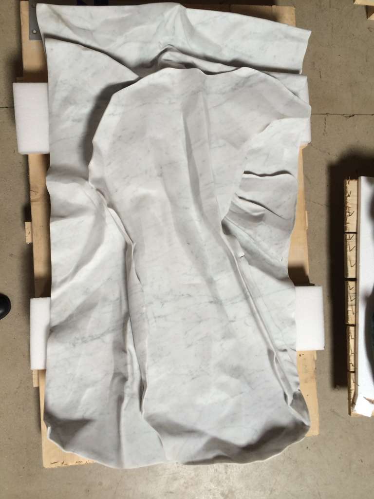 Large white Carrara marble drape carved as crumpled fabric, photographed from above on a wooden pallet
