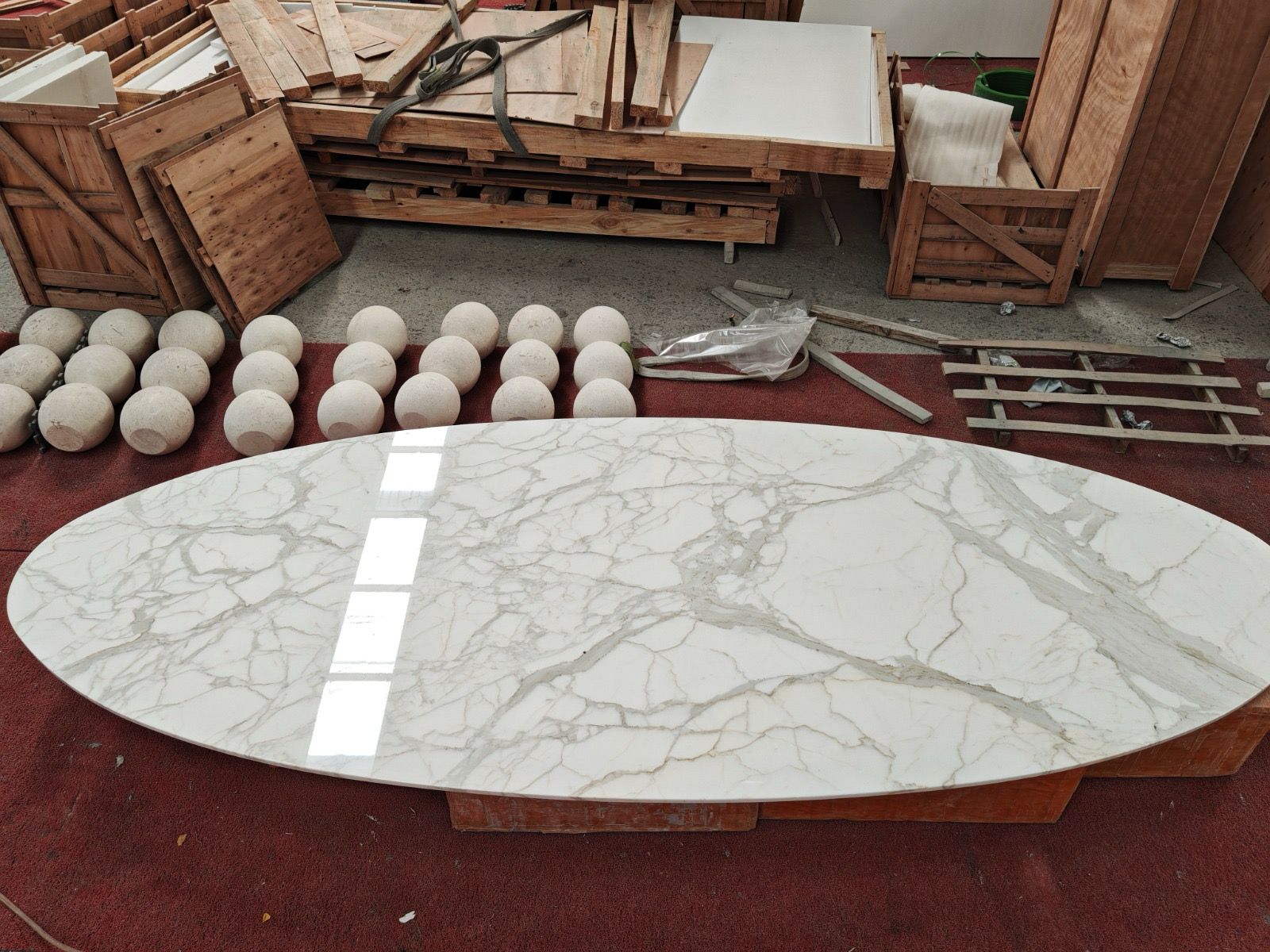 Polished oval Calacatta marble tabletop with bold grey veining, in the workshop with travertine spheres