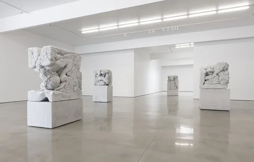 Gallery installation — four monumental carved marble blocks on white plinths in a luminous white-walled room
