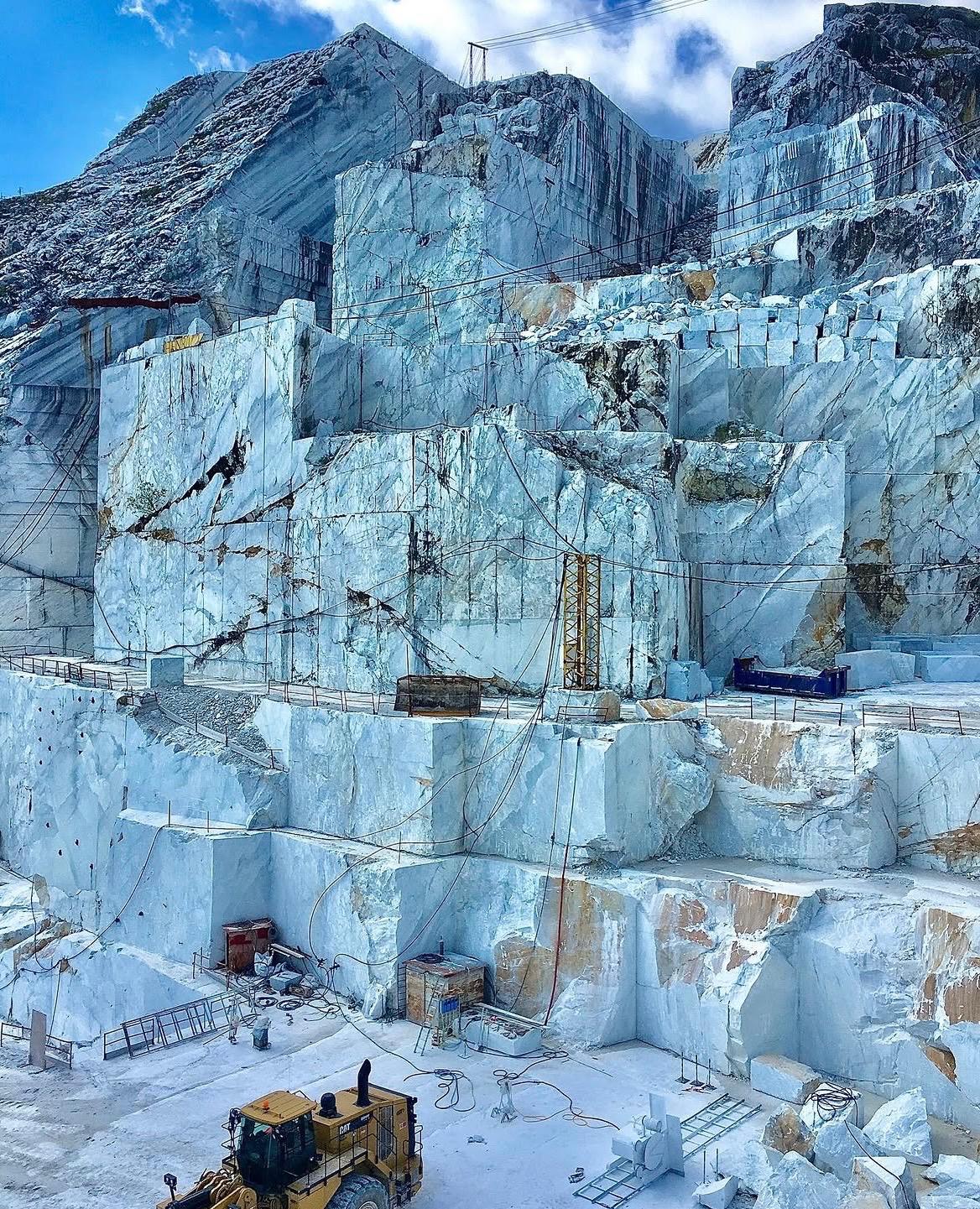Towering walls of a Carrara marble quarry with cut blocks stacked at the base