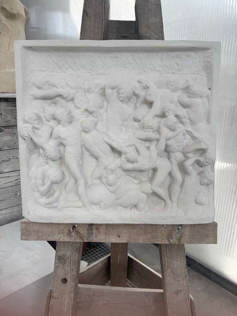 Carved marble bas-relief panel of dancing classical figures, displayed on a wooden easel in the studio
