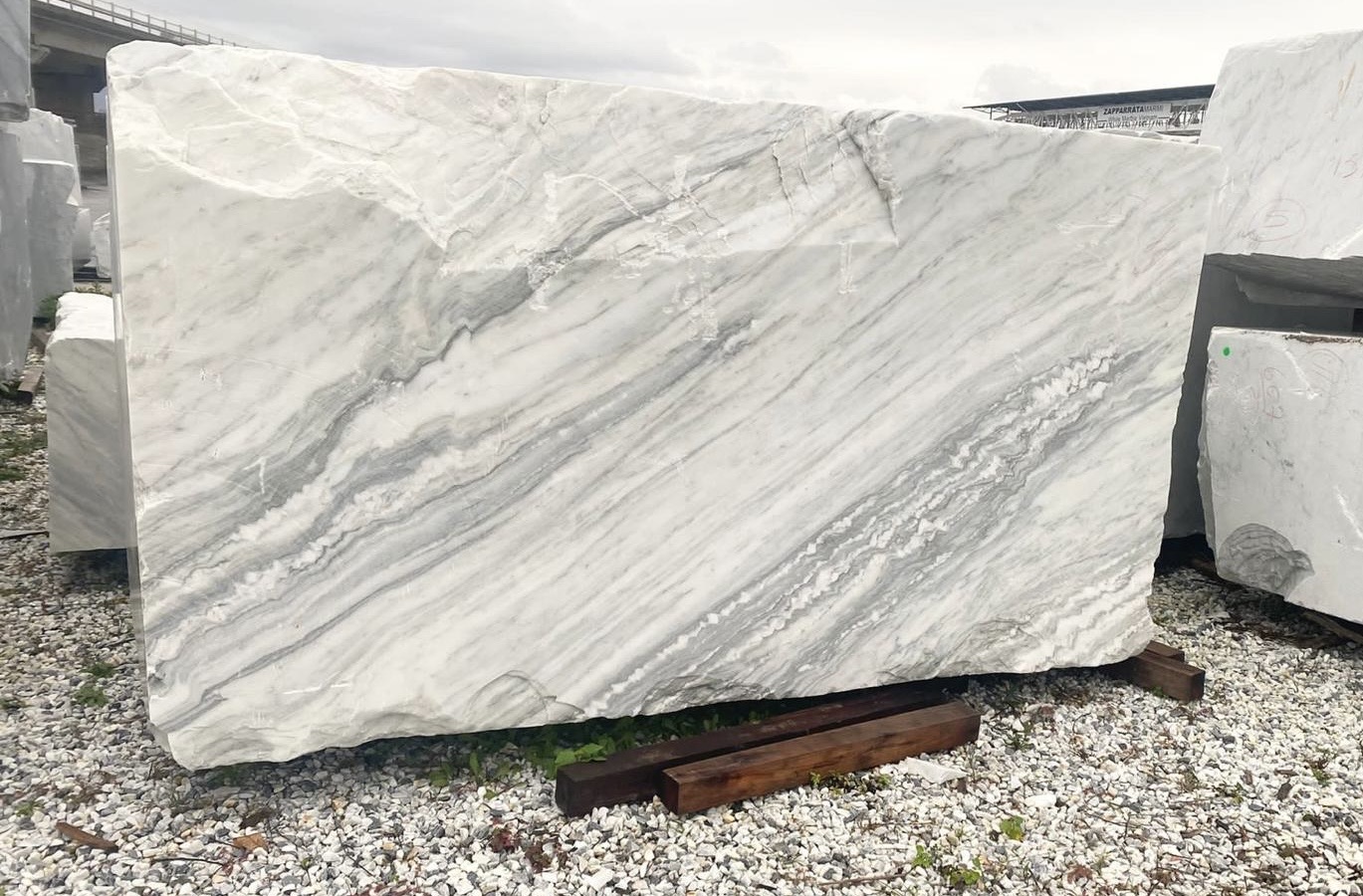 Large slab of white marble with diagonal grey veining, standing in the quarry yard