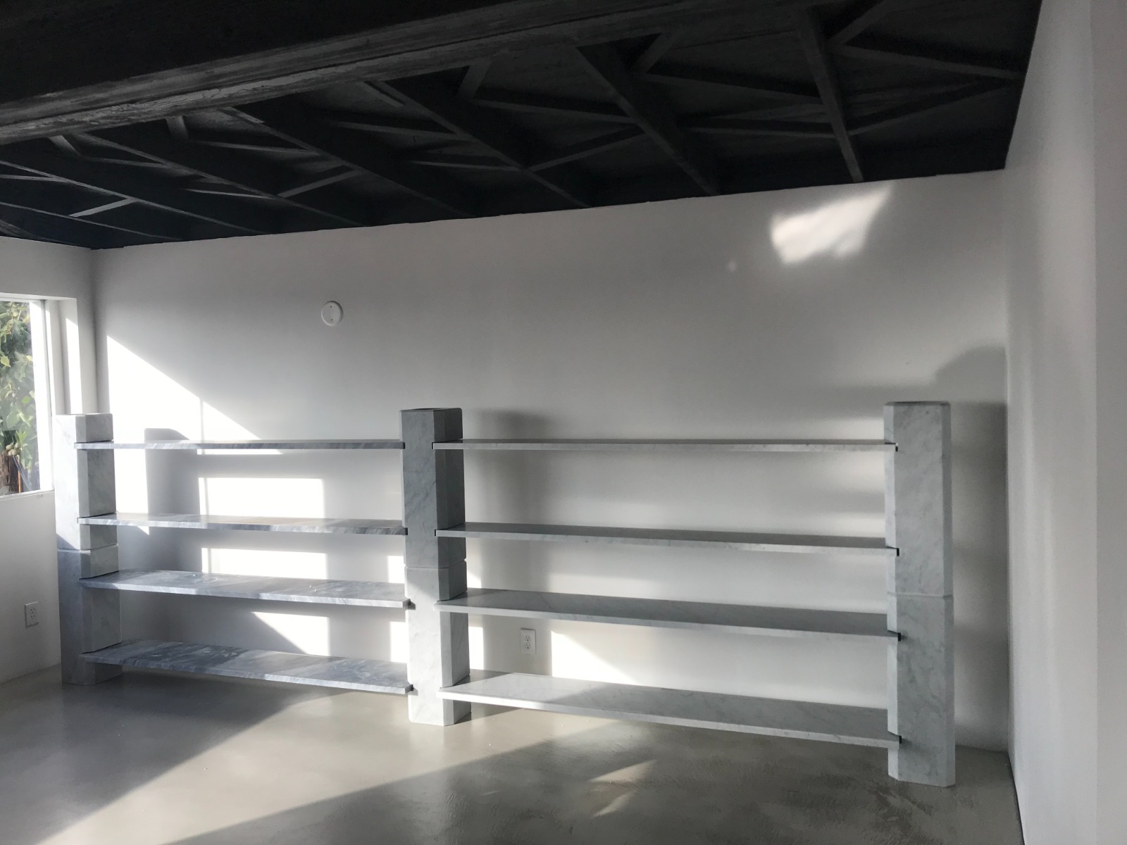Long Carrara marble shelving unit with thick column supports installed along a white wall under a dark coffered ceiling