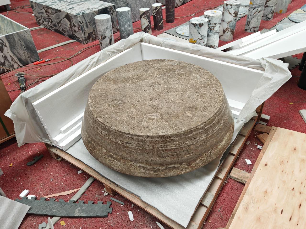 Large circular monolithic travertine disc with concentric tooling rings, crated in the workshop on a red floor