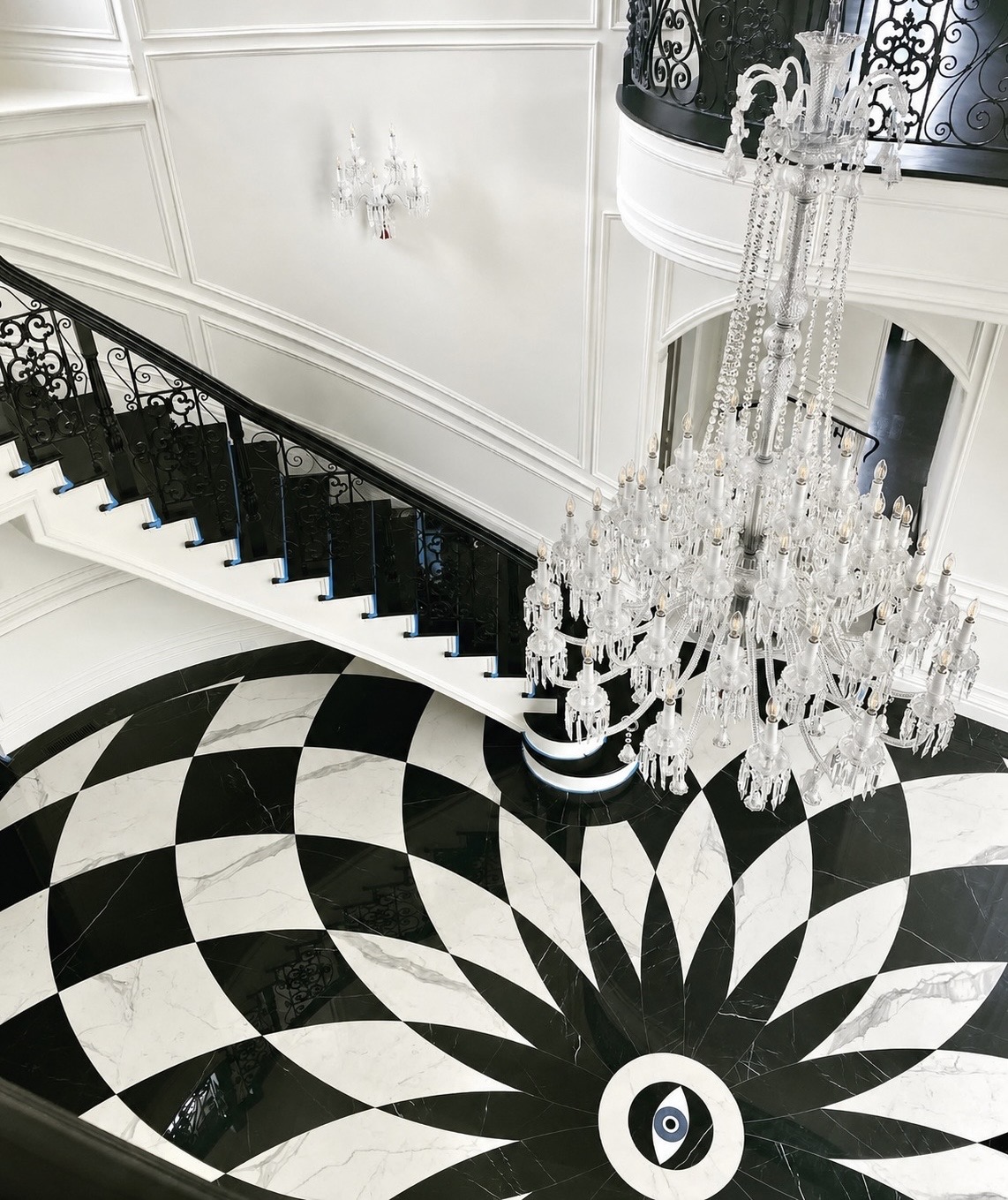 Grand entry hall with a sweeping black-and-white checkerboard marble floor, crystal chandelier, and curved staircase