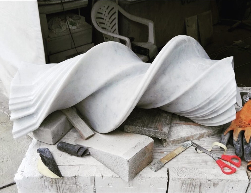 Compact white marble twist sculpture resting on a workbench among tools and sanding blocks