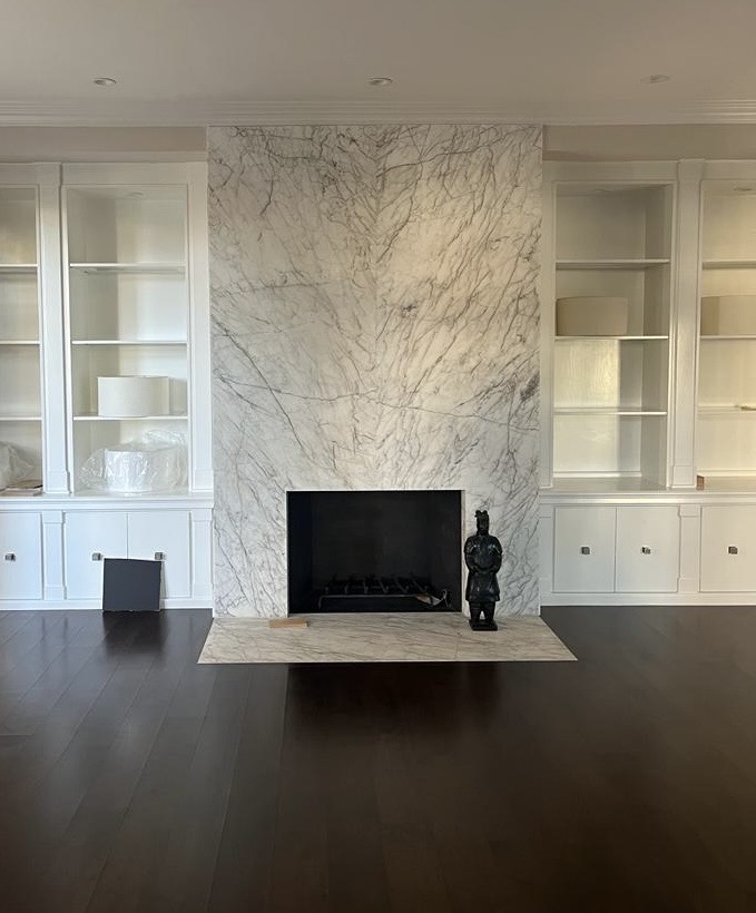 A custom floor-to-ceiling fireplace surround crafted from finely veined Venatino Carrara marble, installed within bespoke built-in bookshelves in a private residence
