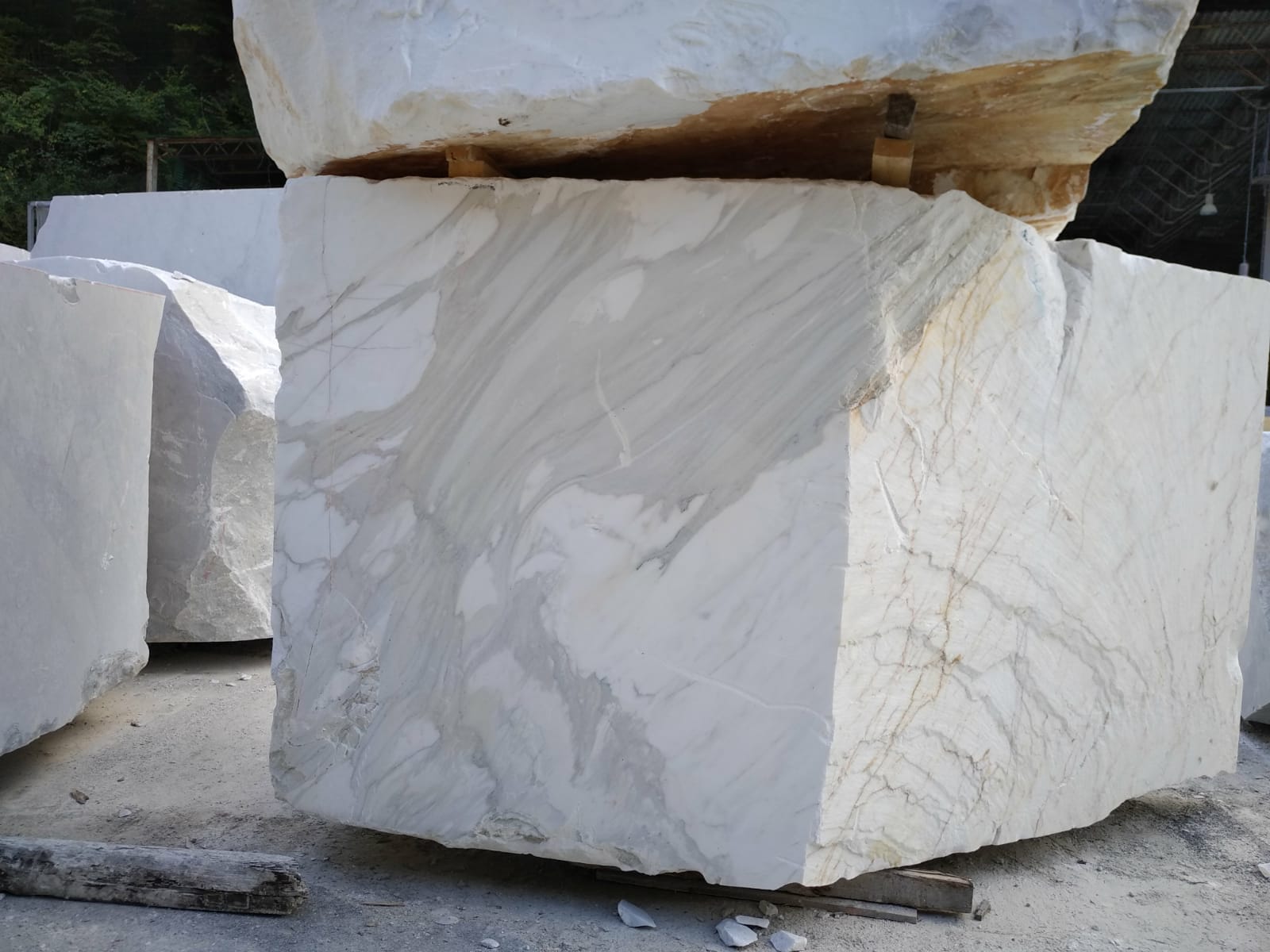 Raw block of Calacatta marble with bold grey and gold feathered veining, stored in the Carrara quarry yard