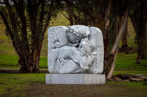 Monumental marble sculpture of two embracing figures set in a landscape of eucalyptus trees