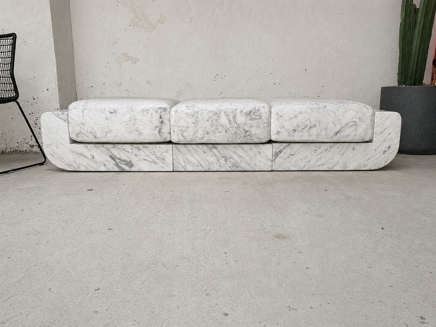 Low sofa sculpted from Statuary Venatino marble with three cushioned seat forms resting on a curved marble base, photographed in a gallery space