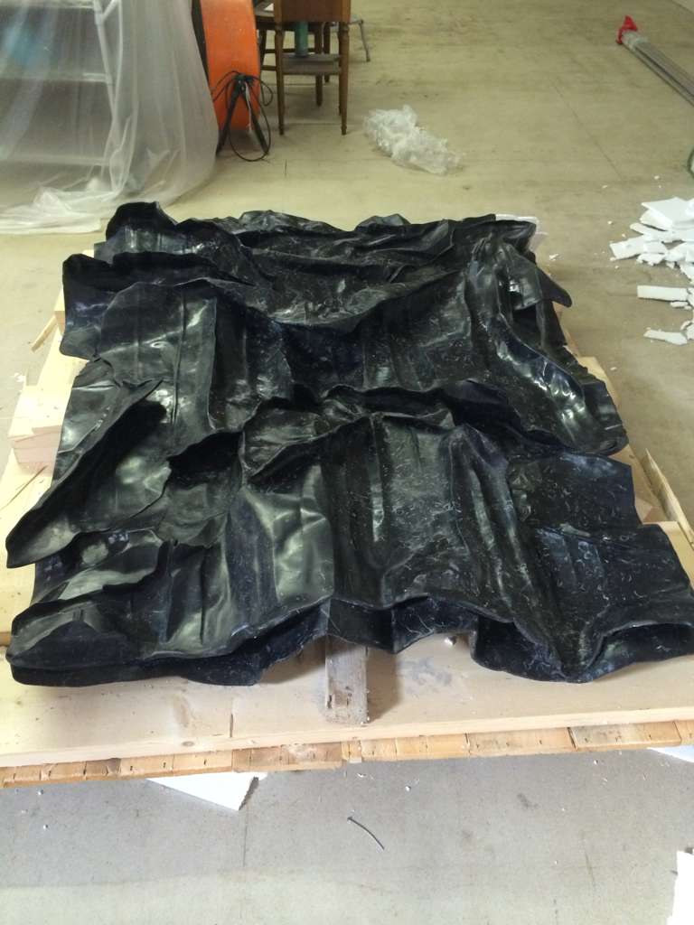 Large black marble drape — a single slab carved into deep folds of cloth, photographed from the front