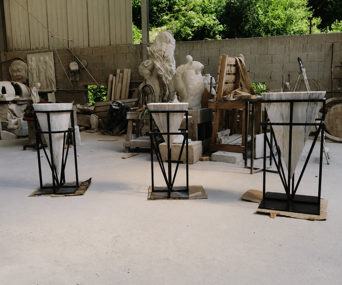 Three inverted white marble cone vessels mounted in black metal stands inside the workshop