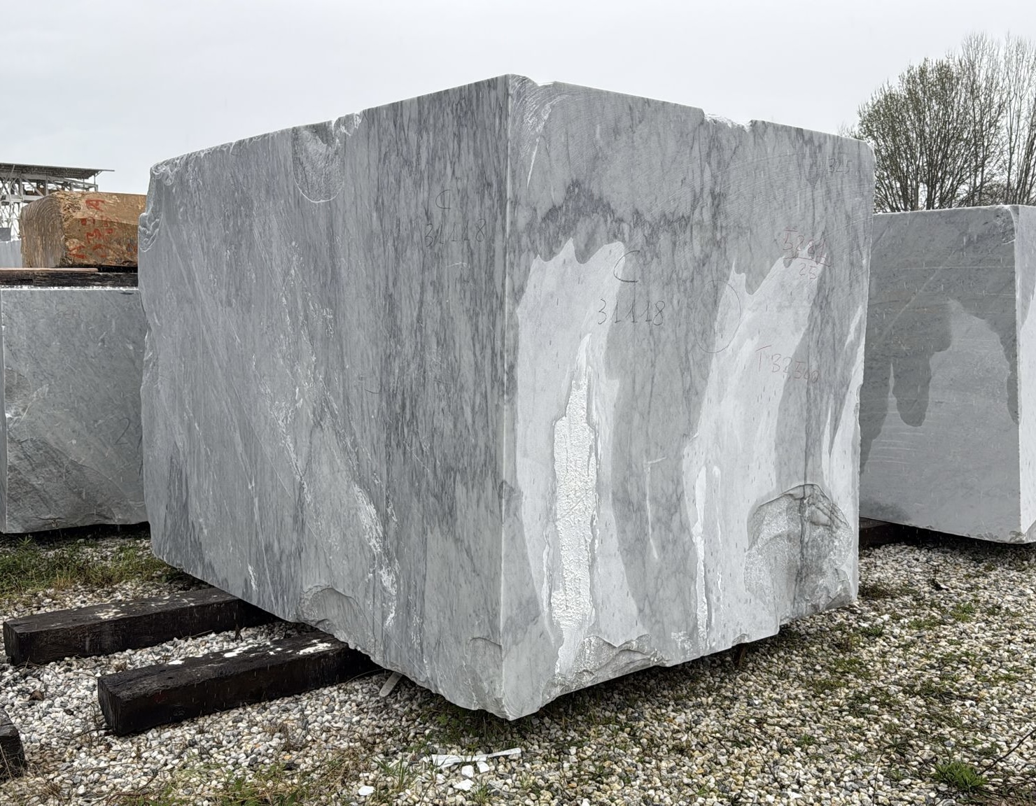 Large squared raw block of Bardiglio grey marble with soft cloud-like veining, stored in the quarry yard