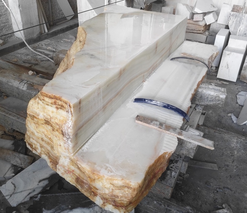 Long white onyx bench with raw quarried edges and a polished top resting on workshop trestles