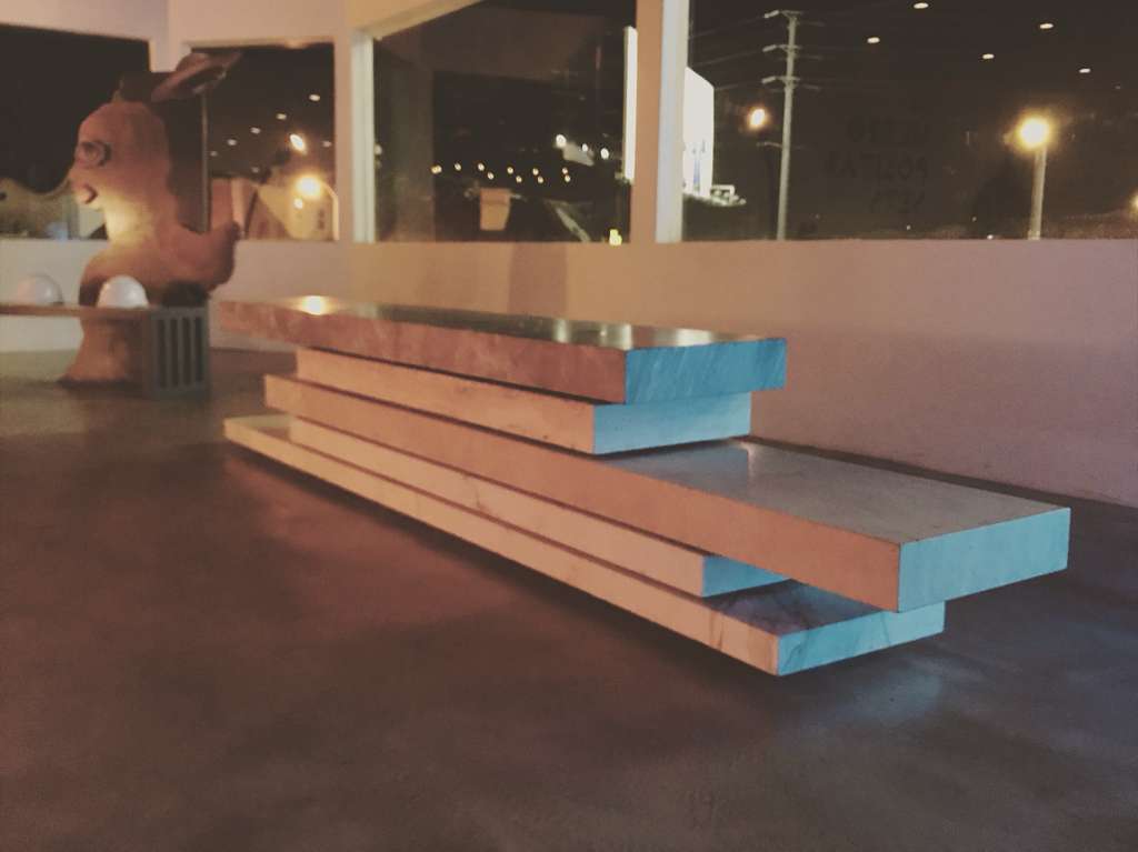 Long horizontal bench of stacked marble slabs in copper, peach and pale blue, photographed at night against a window