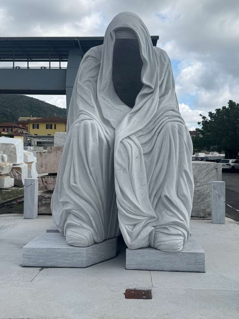 Monumental seated marble figure entirely shrouded in a carved veil, front view in the marble yard