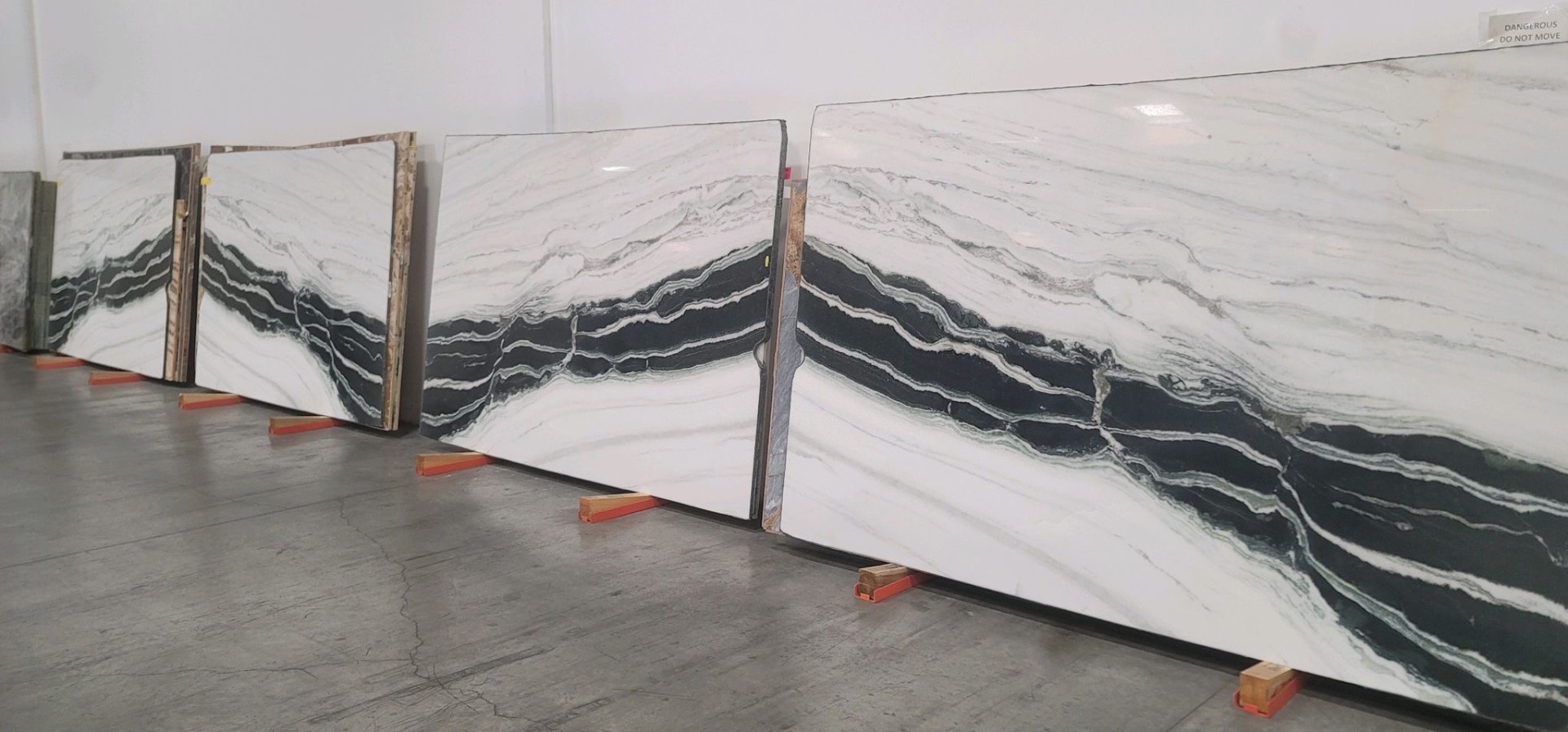 Row of large Panda White marble slabs with dramatic black mountain-like veining, standing on wooden blocks in the warehouse