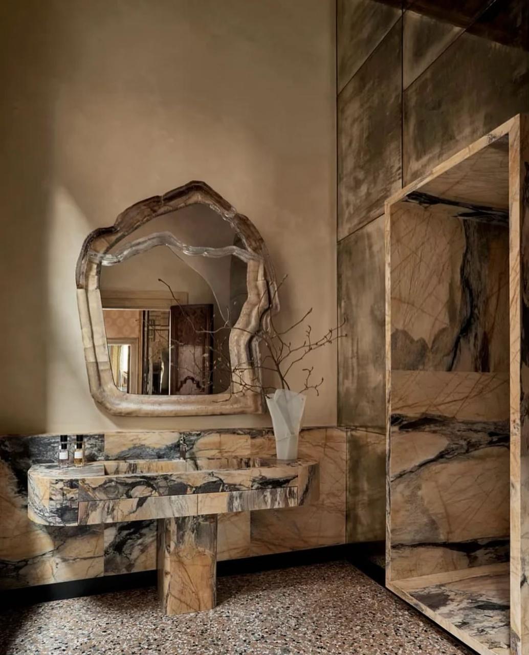 Bathroom interior with organic-edged marble mirror, Giallo Siena sink on a single marble leg, and a marble-framed shower
