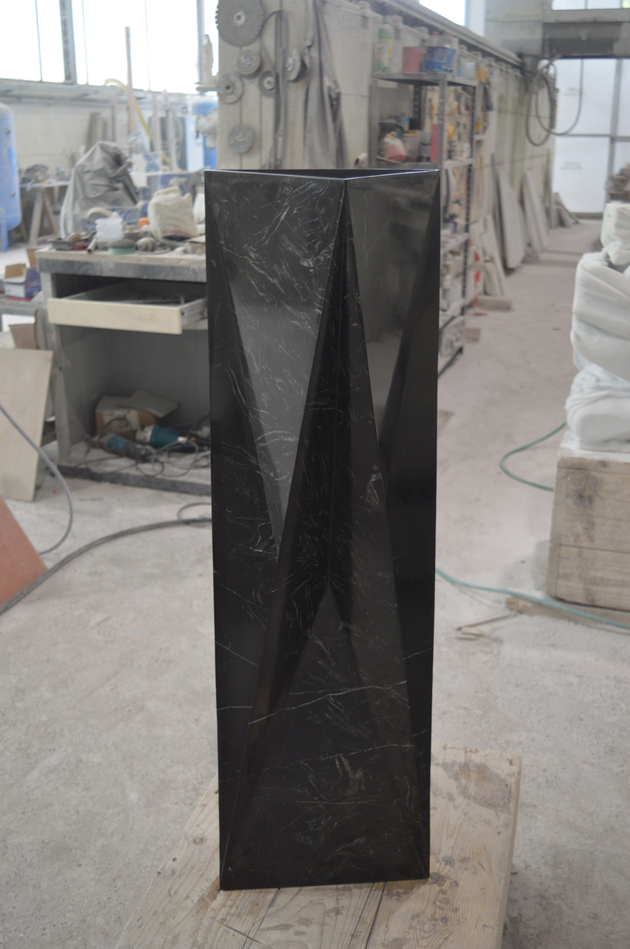 Tall faceted black marble obelisk with sharp angular folds, standing in the workshop