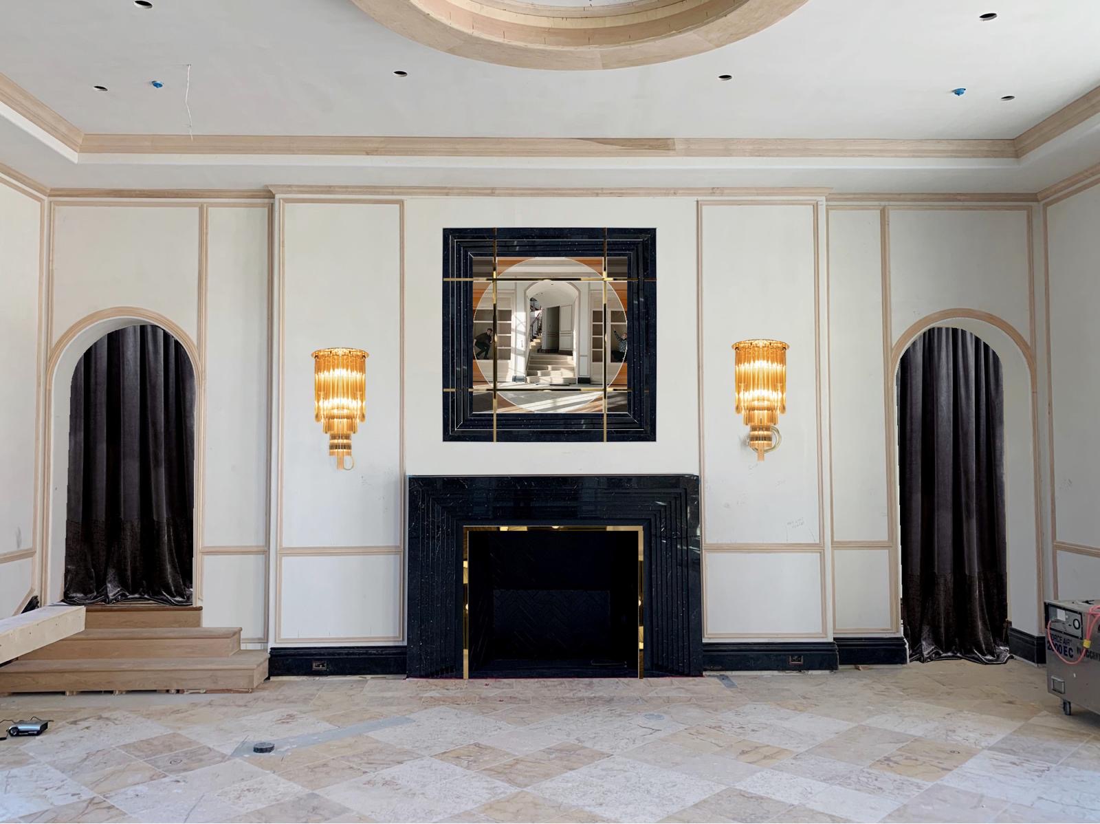 Black Nero Marquina marble fireplace with brass inlay and matching overmantel mirror in a grand room with arched curtained niches and amber sconces