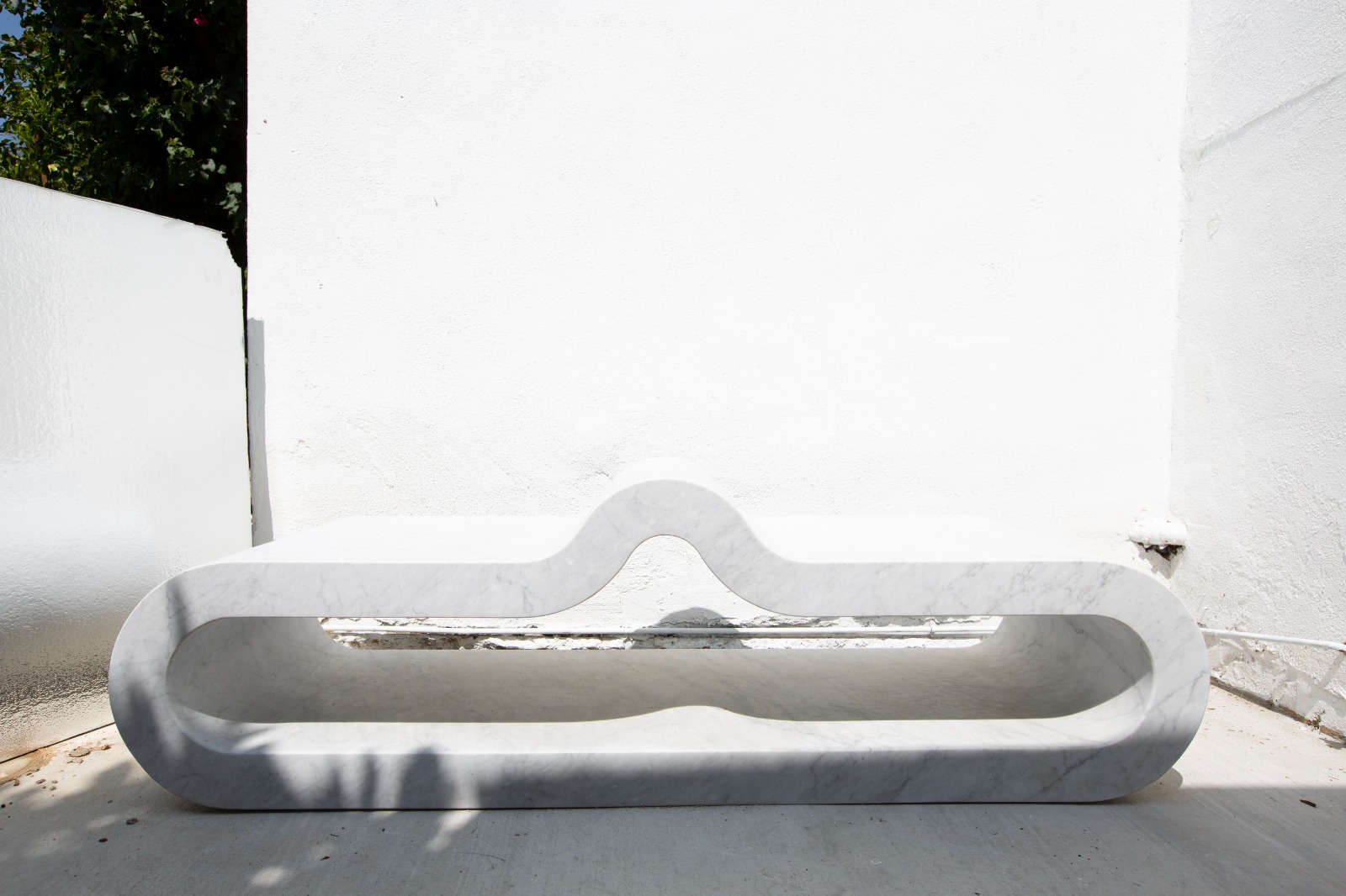 Front view of a carved Carrara marble bench with a continuous wave profile, against a white plaster wall