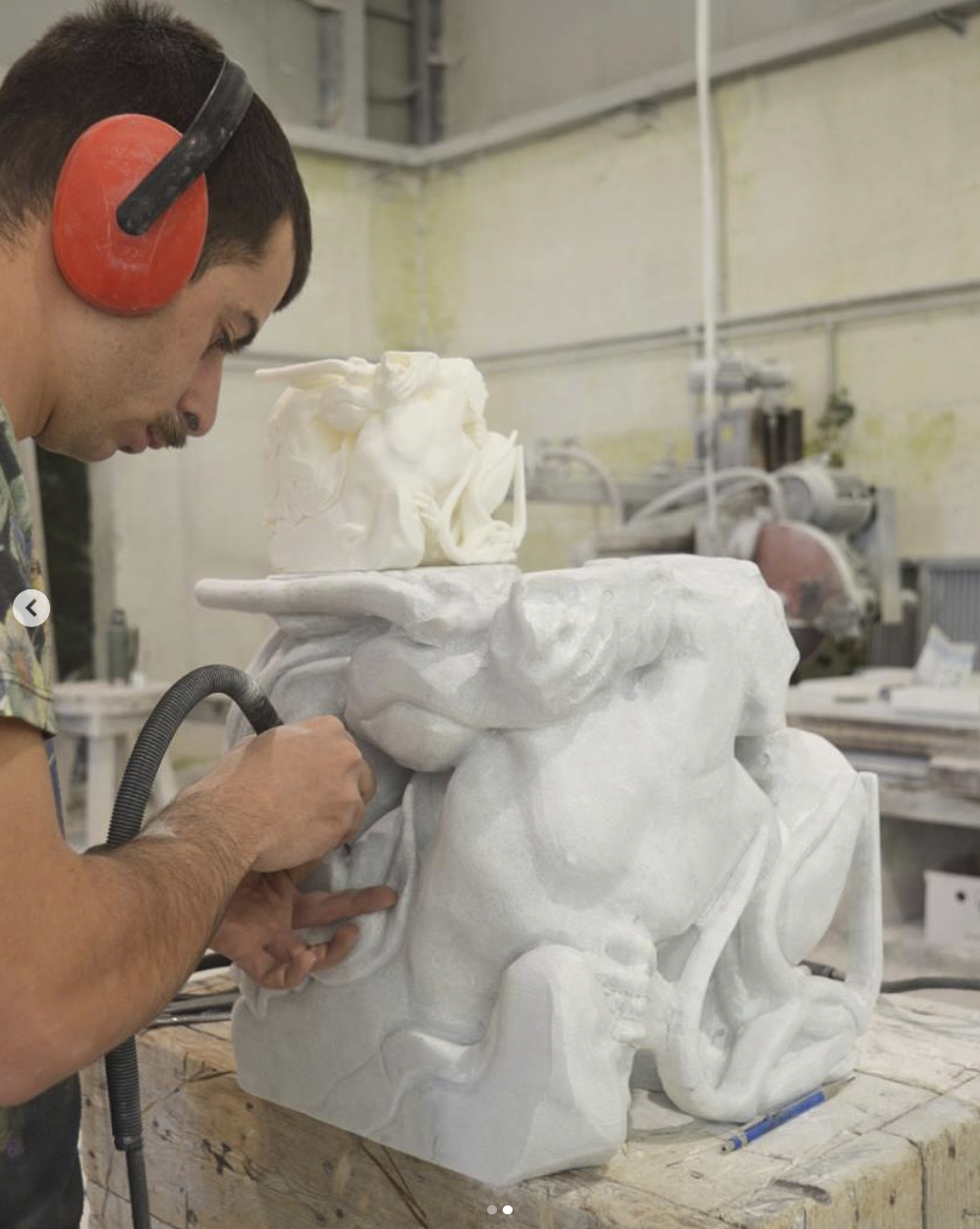 Sculptor carving a marble group of horses, with the small maquette placed on top of the block