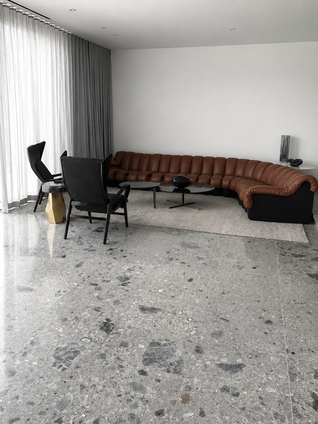 Living room with polished grey terrazzo-like marble flooring, a curved brown sectional sofa, and sculptural black furniture