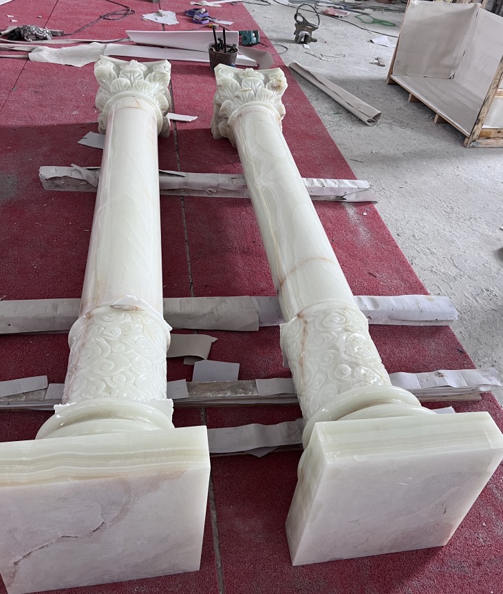 Pair of pale green onyx columns with carved Corinthian capitals and floral collars, lying on a red workshop floor