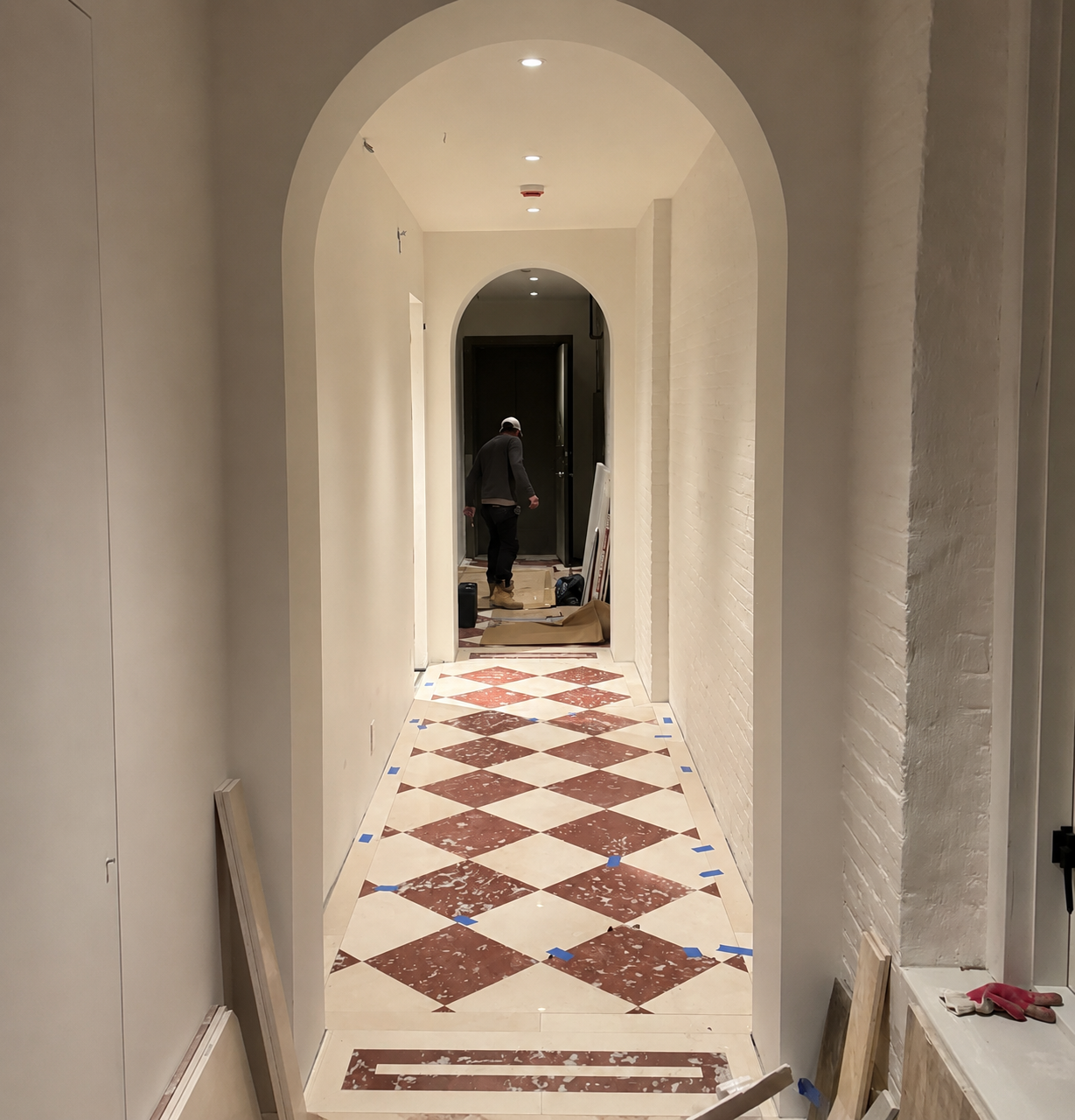 Long interior corridor with arches and a red and cream checkerboard marble floor under installation