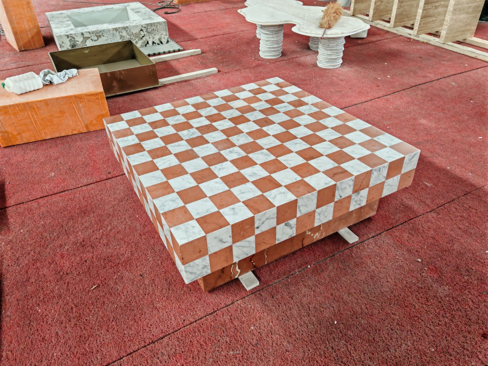 Square coffee table with a checkerboard top in white Carrara and red Rosso marble tiles, on a red workshop floor