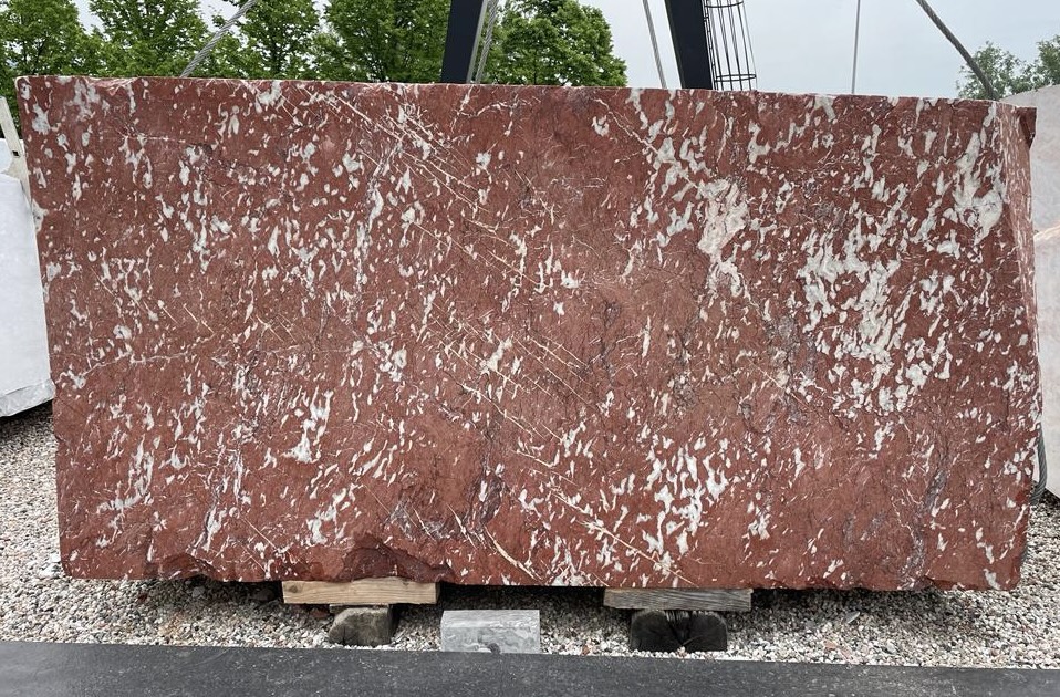 Raw slab of Rosso Francia marble with deep red body and dense white veining, resting in the stone yard