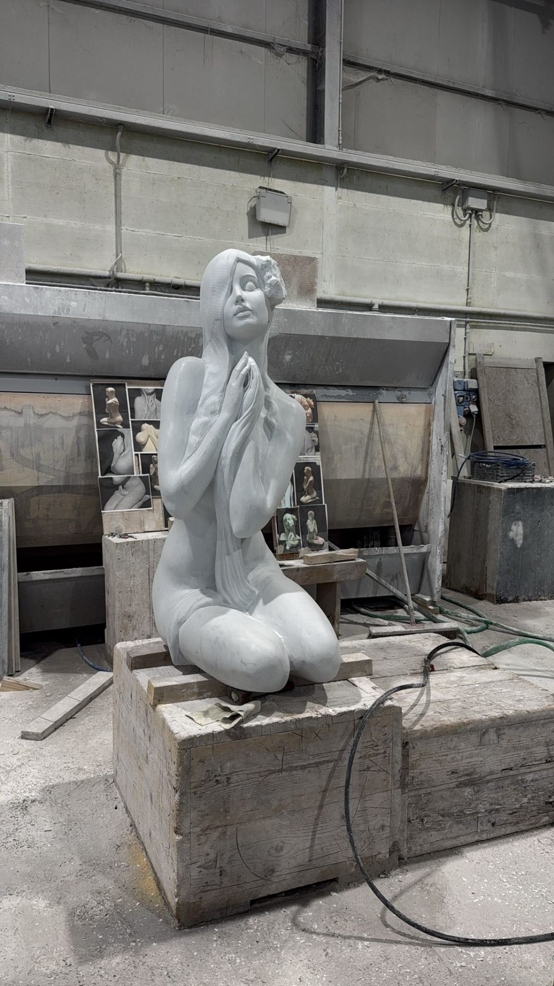 Monumental kneeling female marble figure in the workshop, with reference photos pinned behind