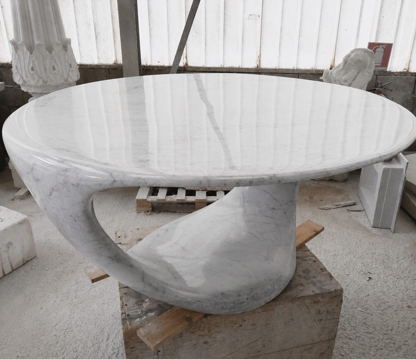Large round white marble table with a sculpted looping pedestal photographed in the workshop