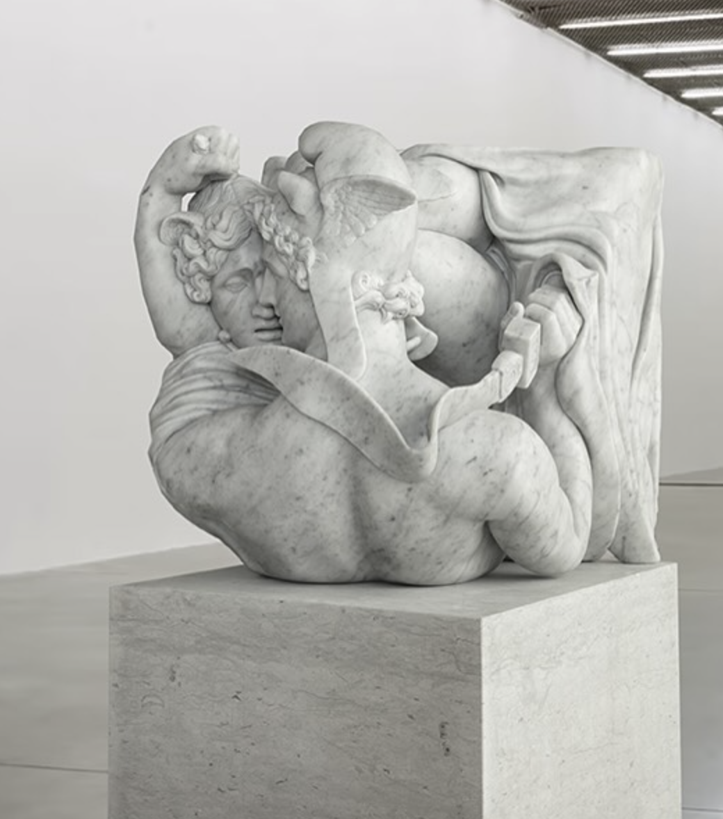 Classical marble sculpture of two embracing winged figures on a travertine plinth in a gallery