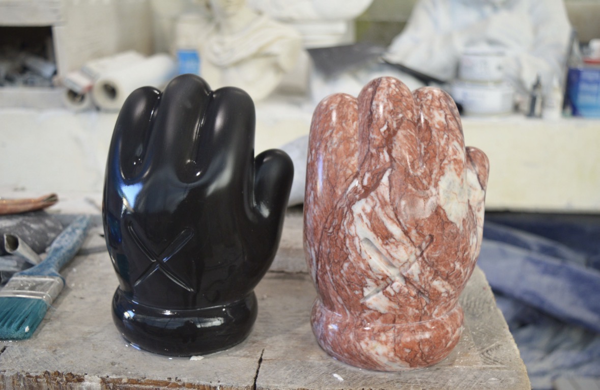 Two carved marble hands — one in glossy black, one in rosso veined marble