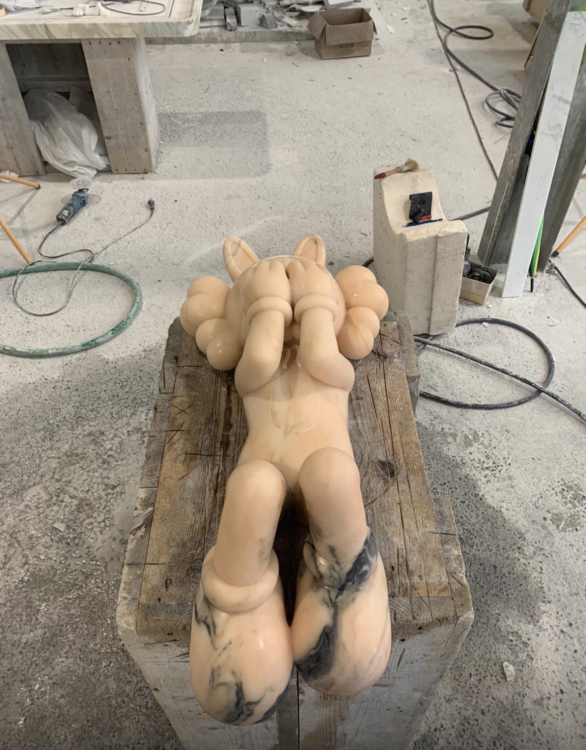 Back view of a large peach marble reclining KAWS Companion figure with dark marble feet
