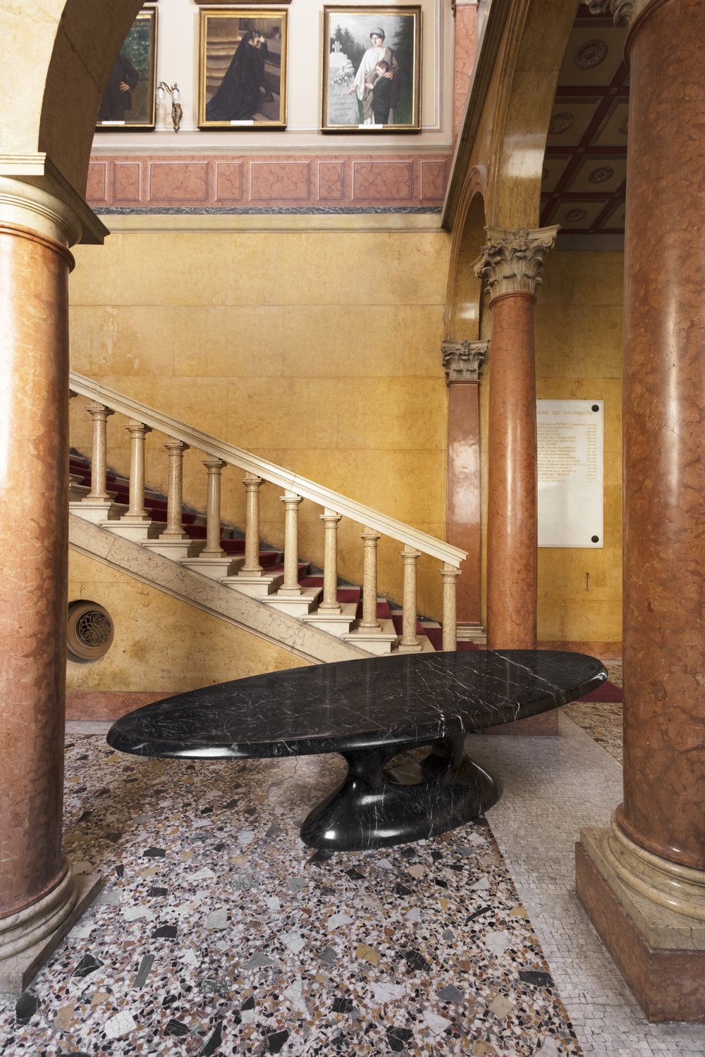 Oval black marble table in a classical palazzo hall with terrazzo floor