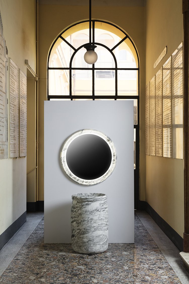 A round marble-framed mirror above a cylindrical marble sink in a palazzo corridor